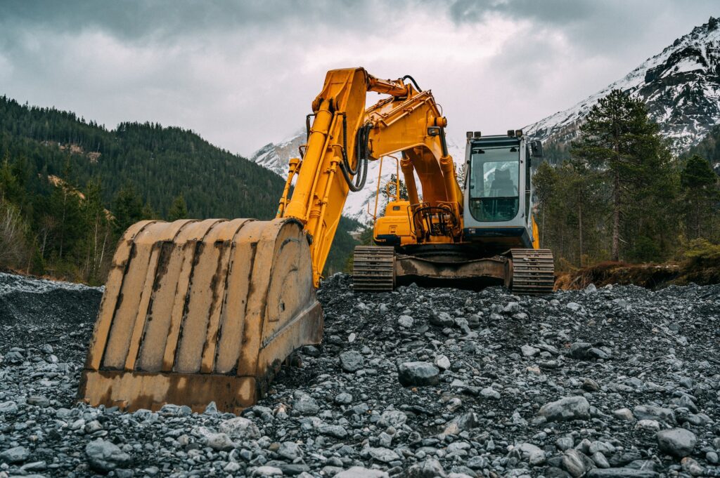 Yellow excavator sitting on a pile of rocks in mountainous area